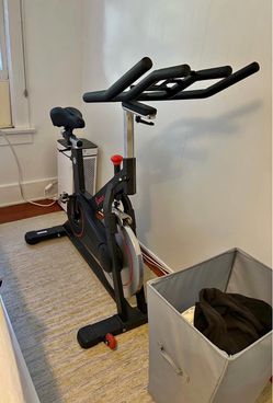 Sturdy black Sunny spin bike has red accents. Bike has adjustable seat and handlebars. Pedals are SPD compatible.