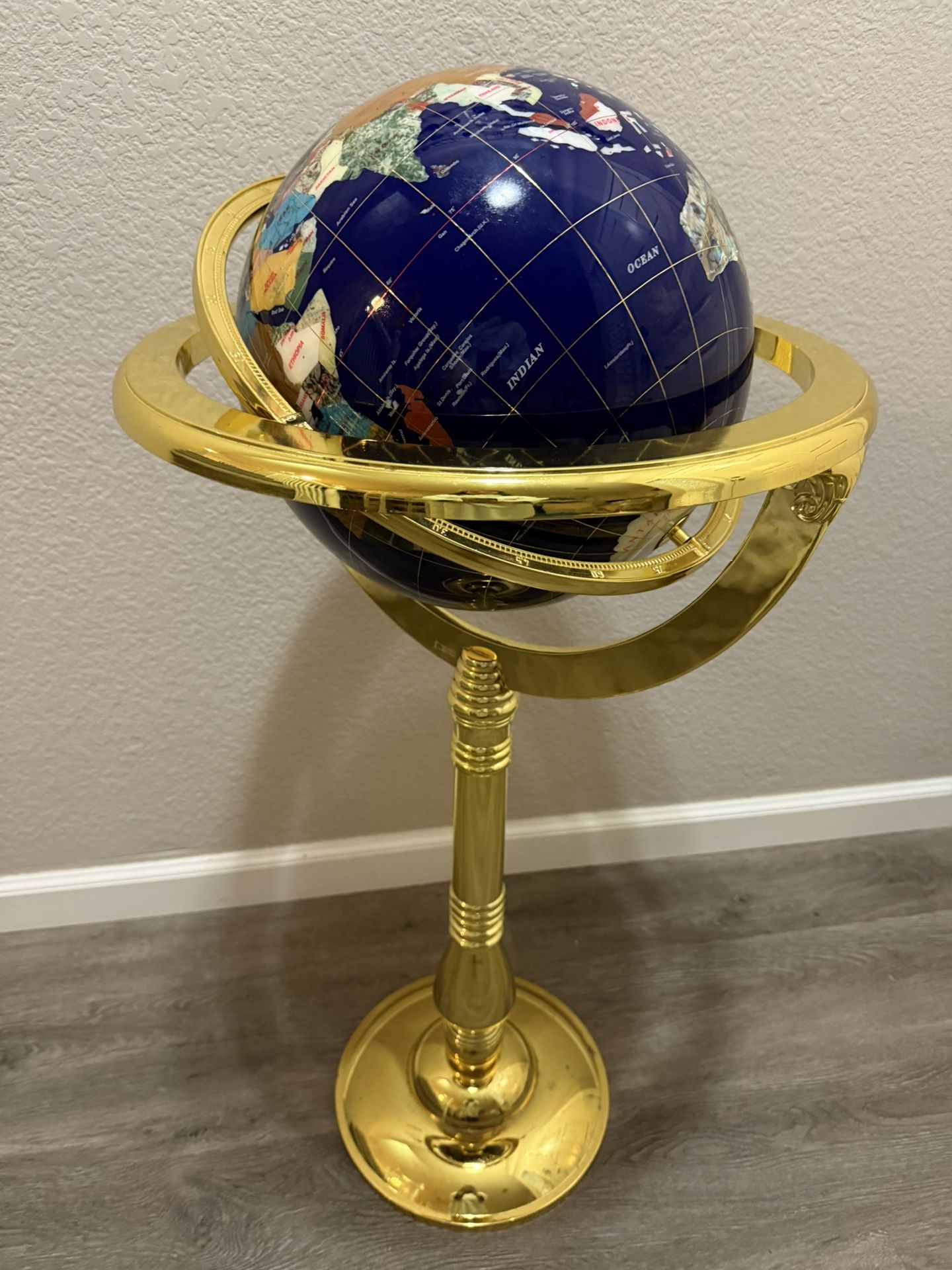 GEMSTONE GLOBE ON BRASS FLOOR STAND Eighteen different gemstones on a blue lapis lazuli ground. Height of stand 43". Diameter of globe 13". Small area