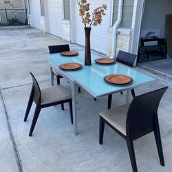 Expandable metal and glass dining table with 4 contemporary wood and fabric chairs.