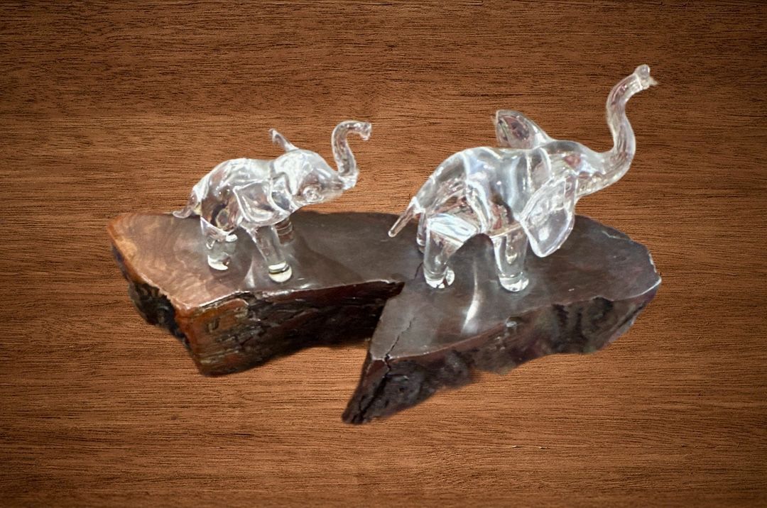Clear glass decorative elephant on a wooden base, with its trunks raised for good luck