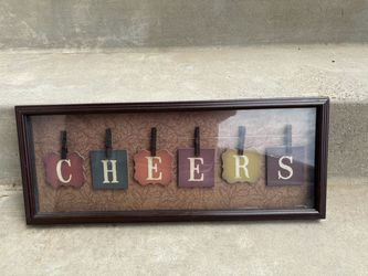 framed wall art piece featuring the word "CHEERS" spelled out on individual wooden plaque tags clipped with miniature clothespins