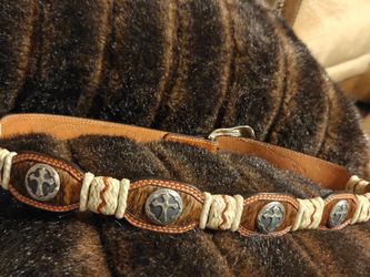brown leather belt features distinctive cross conchos and white braided detailing