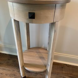 Round Wooden Table With Curved Drawer , Lower Shelf. In Light Wood grain Finish, Metal Accents On Legs.