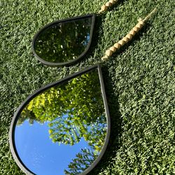teardrop-shaped mirror with a black frame and decorative wooden bead