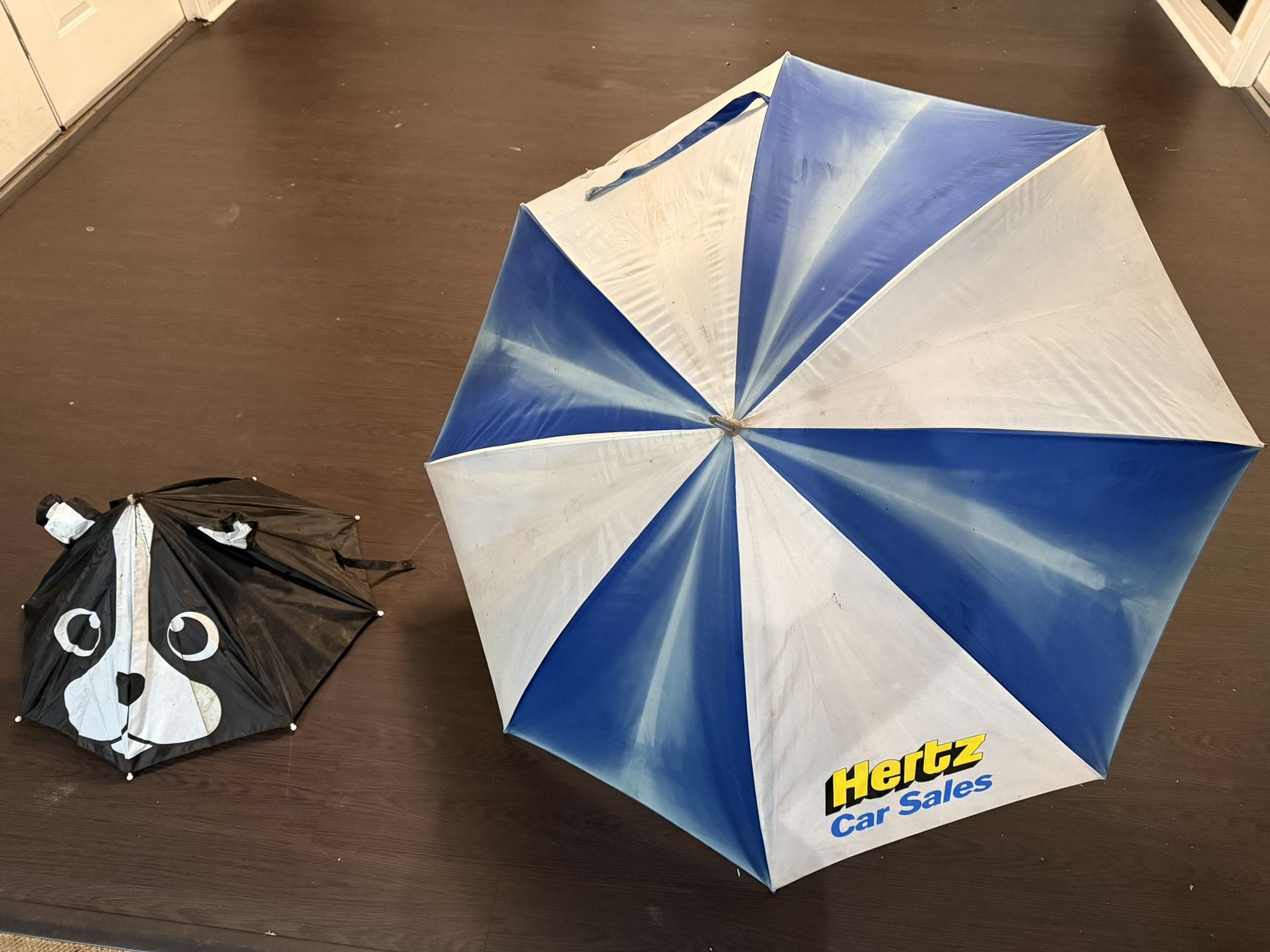 Large blue and white Hertz Car Sales umbrella and small animal face umbrella.