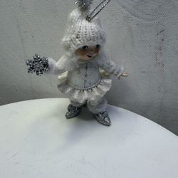 This item is a vintage or collectible Christmas tree ornament depicting a little girl in a winter outfit. The figurine is crafted in white and silver 