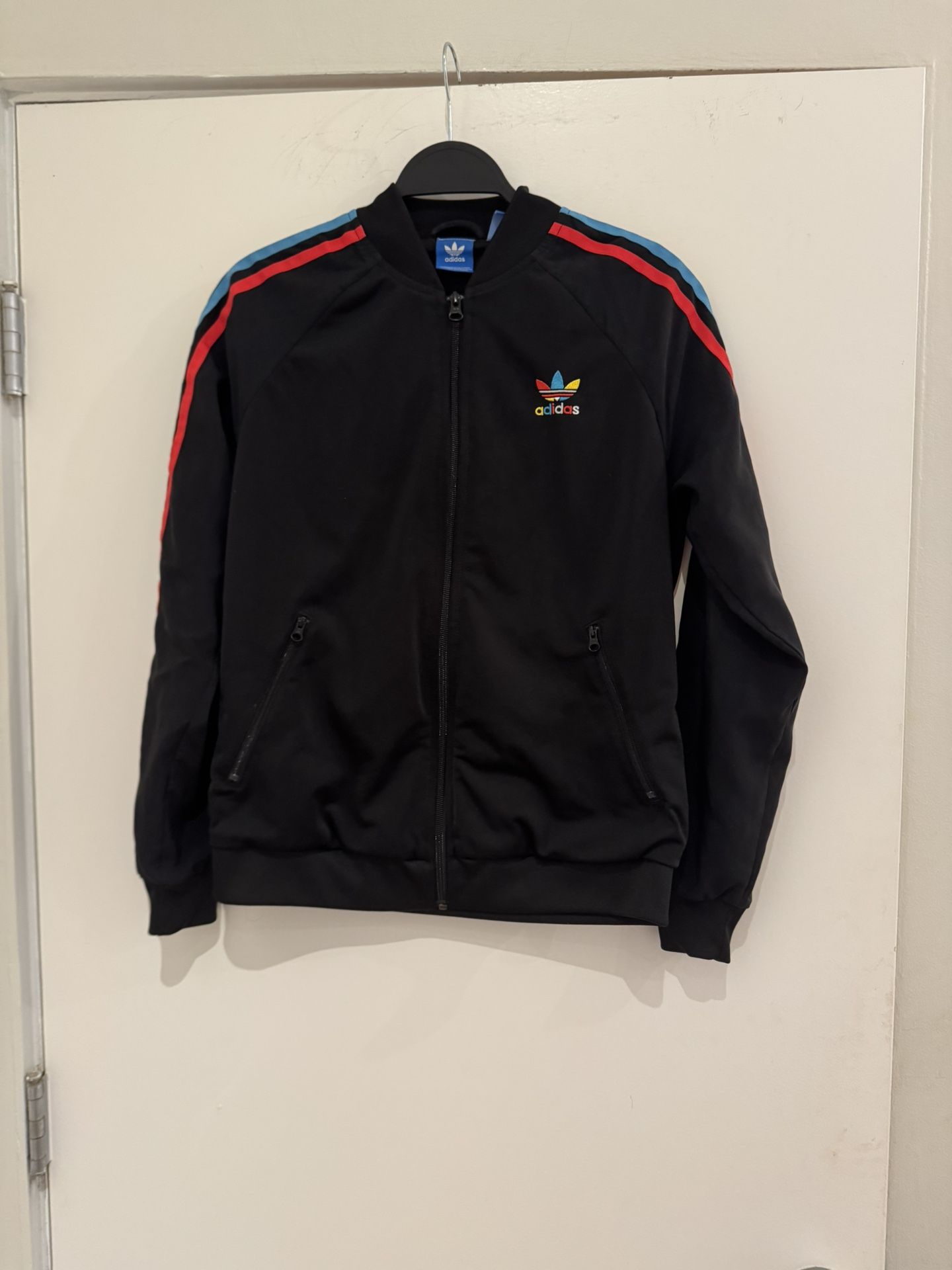 Worn once.Sleek black bomber jacket with vibrant red and blue shoulder stripes. Features iconic Adidas logo. Perfect for casual wear.