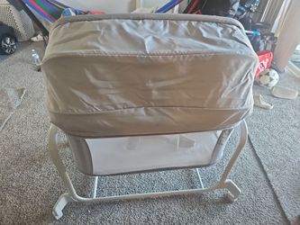 gray baby bedside bassinet with a canopy, mesh sides, wheels, and an electronic control panel.