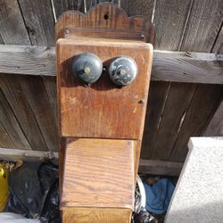 This is an antique wood hand-crank wall telephone, likely from the early 1900s. 
It is a collectible item. 
It features a wooden case, dual bells, and
