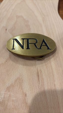 vintage NRA (National Rifle Association) solid brass belt buckle. The buckle is oval-shaped and made of brass, with the letters "NRA" in black enamel