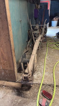 antique, horse-drawn wooden walking plow  breaking plow resting inside a barn, featuring a long wooden beam and a cast-iron adjustment quadrant at the
