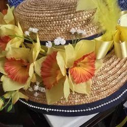 Boater hat with a dark ribbon, a pearl-like trim, and a bouquet of yellow & peach flowers & feathers