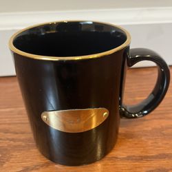 Black Coffee Mug, With Gold Rim And R C On A Gold Piece Of Metal Attached To The Cup