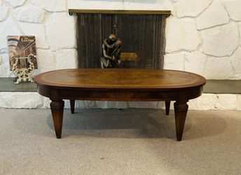 vintage oval coffee table with a gilt-tooled leather top, likely made of mahogany or walnut. 