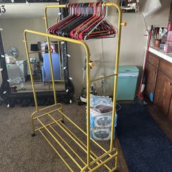 yellow metal double rod garment rack on wheels, designed for hanging clothes and providing additional shoe storage on its bottom shelves. 