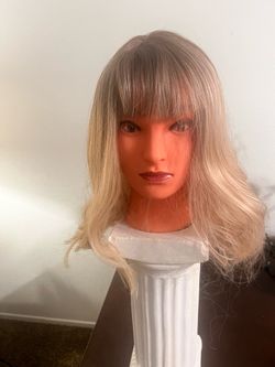 Stylish blonde wig has a wavy texture and full bangs. This shoulder-length hairpiece features a dark root transition into a light blonde shade. It is 