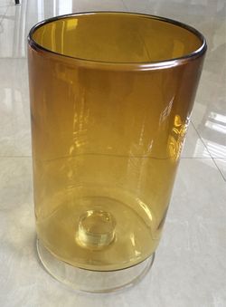 Amber glass vase with a clear glass base. This piece is made of thick glass and has a cylindrical shape with an internal candle pedestal.