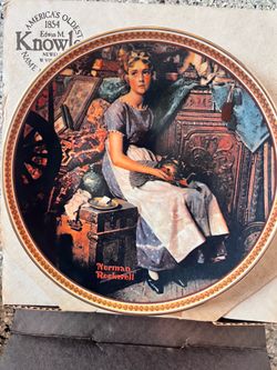 This vintage Edwin M. Knowles porcelain collector plate features the "Dreaming in the Attic" artwork by Norman Rockwell, framed by a decorative gold b