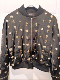 This is the AKIRA Label "Like A Charm" Embellished Bomber Jacket, featuring various gold-toned heart and cross charms.