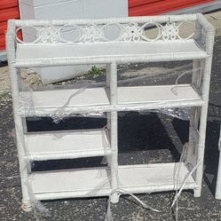 Three tiered white wicker shelving unit,  classic bohemian  aesthetic, with a lattice patterned gallery at the top.  Rattan wicker