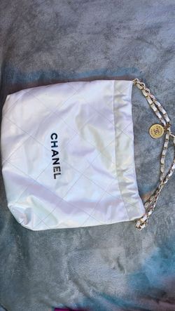 white Chanel 22 hobo bag featuring diamond quilting, gold-tone chain straps, and black metal logo lettering