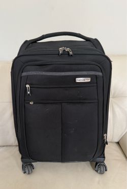 This black Samsonite spinner suitcase features a front-facing silver logo badge and durable soft-side polyester construction