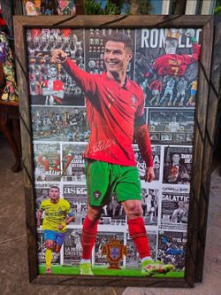 A wood-framed decorative picture featuring a collage of photos, trophies, and press clippings of footballer Cristiano Ronaldo