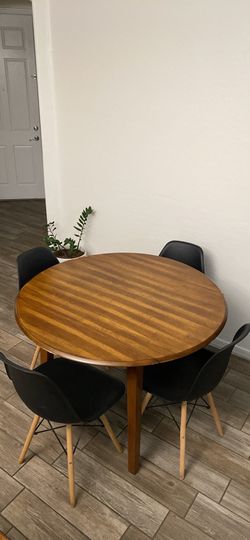 Wooden round dining table with four black chairs.