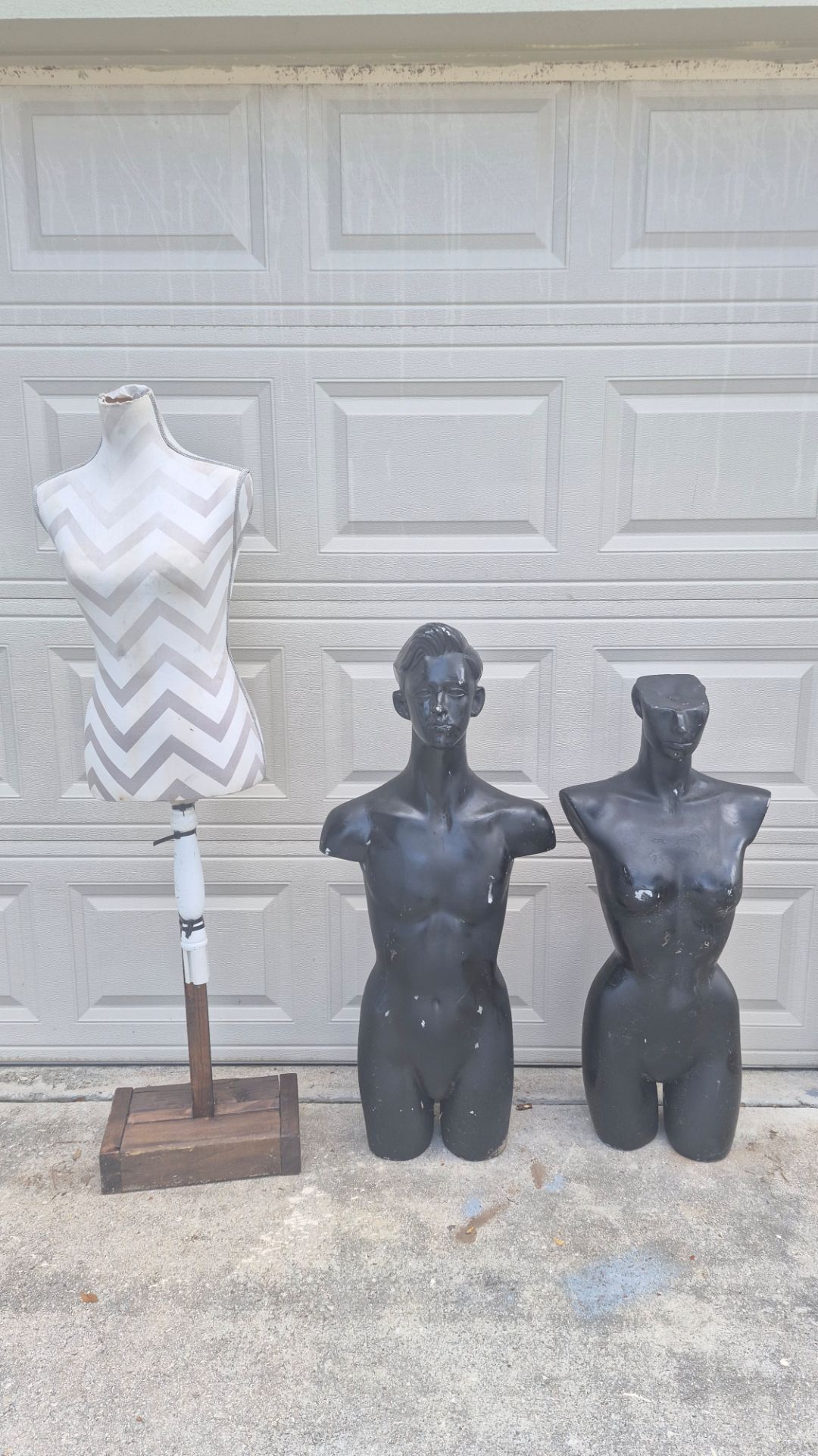 Versatile set of three display mannequins. One dress form has a grey and white chevron fabric cover on a white and brown wooden stand. Two black plast