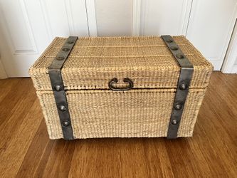 Handwoven rattan storage trunk with steel frame on wheels.