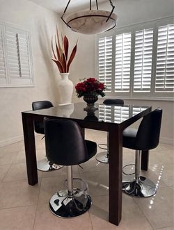 Dark wood pub-height table with glass top (36in H x 48in W+ 4 black faux-leather swivel stools with chrome bases