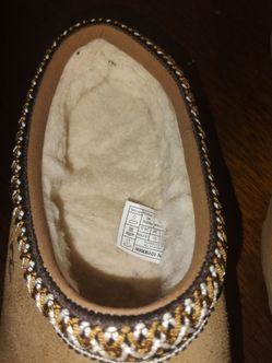 These are the UGG Tasman slippers in chestnut suede, featuring their signature embroidered braid collar.