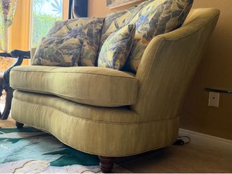 Green fabric loveseat with a curbed silhouette and parrot-patterned throw pillows.