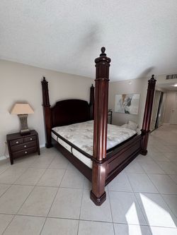 Solid dark cherry wood four-poster bed frame with tall fluted columns, decorative finials, arched headboard, and solid footboard panel. King size. Mat