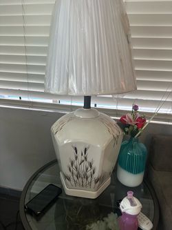 Vintage ceramic table lamp has a cream-colored base with a brown wheat stalk pattern. The lamp includes a pleated fabric shade with a protective plast