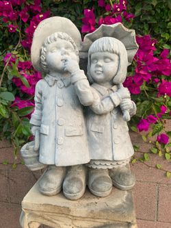 Two kids under umbrella with a water bucket statue