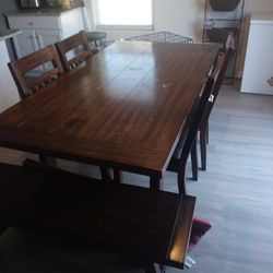 Brown table with 4 chairs and a bench.