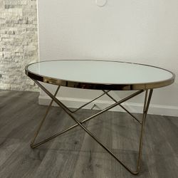 New round modern coffee table with a gold-tone metal base and a glass top 