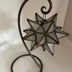 This is a frosted glass and metal Moravian star hanging tea light lantern candle holder with a stand