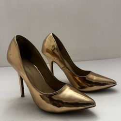 Wild Diva pointed-toe stiletto pumps in a metallic rose gold color. They feature a sleek, patent finish and a high heel. Size 8