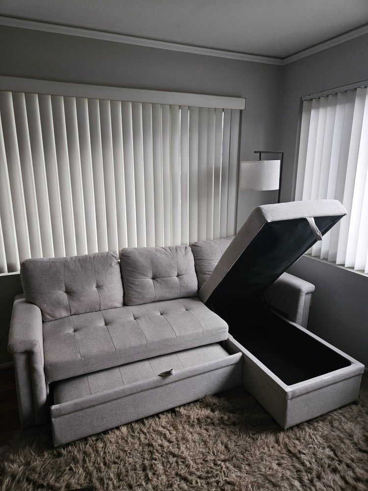 Lilola Home Lucca reversible sleeper sectional sofa with storage chaise in a light gray or beige woven fabric. 