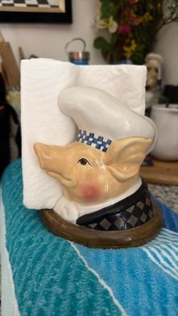 This is a Department 56 Jam Bon chef pig ceramic napkin holder featuring a blue-checked hat and a checkered coat.