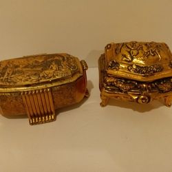 Two ornate gold metal trinket box with engraved scenes. One is 3 1/2” wide and the other is 4 1/2” wide. Red velvet lining. 