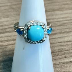 Vintage sterling silver ring featuring a bright turquoise center stone framed by a sparkling halo. Deep blue accent stones on each shoulder add contra