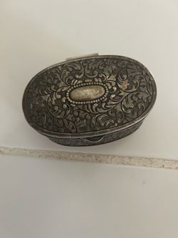 vintage silver-plated oval trinket box featuring an ornate embossed floral and scrollwork design on the lid