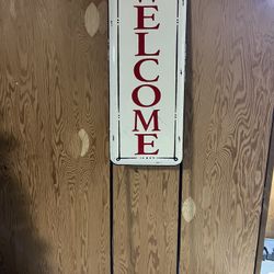 Decorative welcome Metal sign with red lettering.