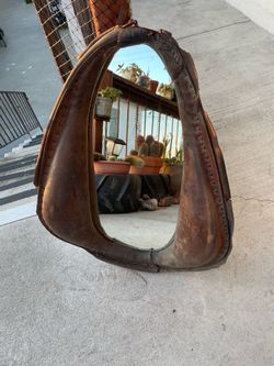 Mirror is fashioned from an antique leather horse collar, often featuring a distinct patina and buckle closure.