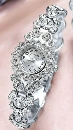 Elegant silver-tone dress watch with a rhinestone-encrusted bezel and bracelet. This timepiece has a round white dial with black Arabic numerals and a