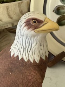 Pride of America Detailed bald eagle statue. Has brown body and white head with yellow beak and feet. Sits on a dark base. Textured feathers on body a