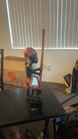 The 18-inch tall hand-carved wooden statue depicts an African figure pounding food in a mortar